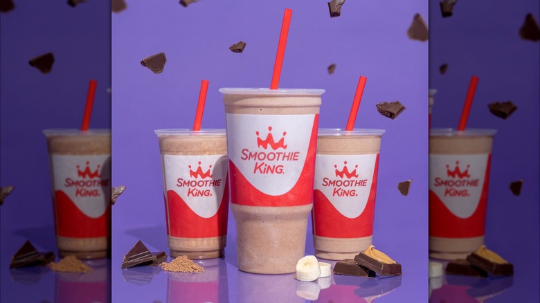 Three Smoothie King smoothies in two sizes with flying chocolate as well as bananas and chocolate on the table
