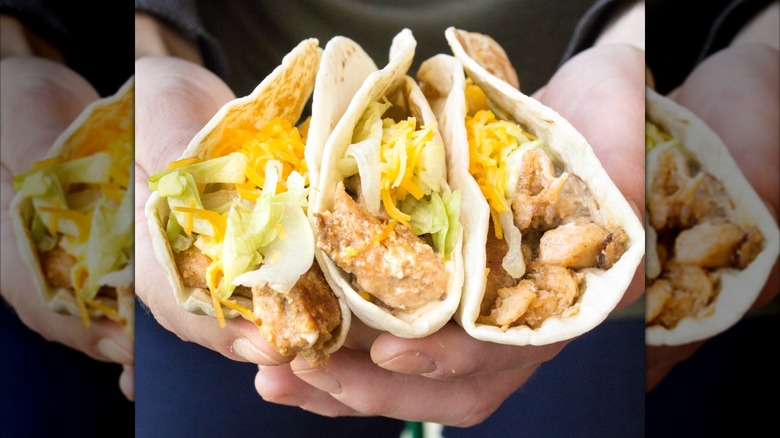 Hands holding three grilled chicken tacos