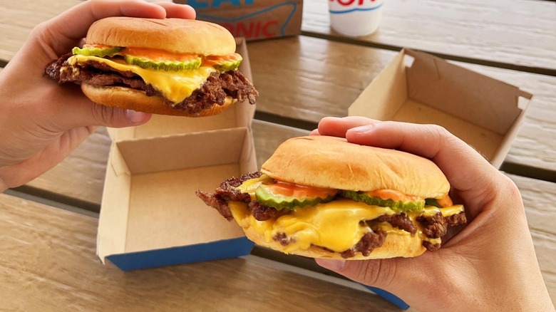 Two hands holding Sonic cheeseburgers