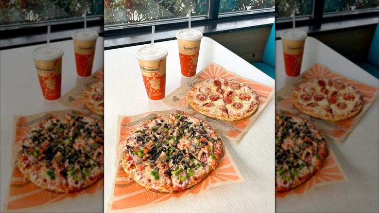 A supreme and a pepperoni Schlotzsky's pizza on a table with drinks