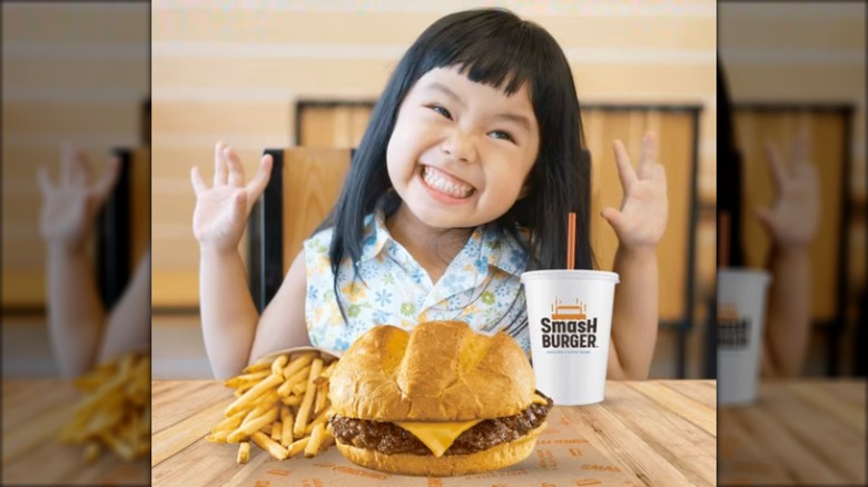 Young girl sitting in front of a hamburger, fries, and drink.