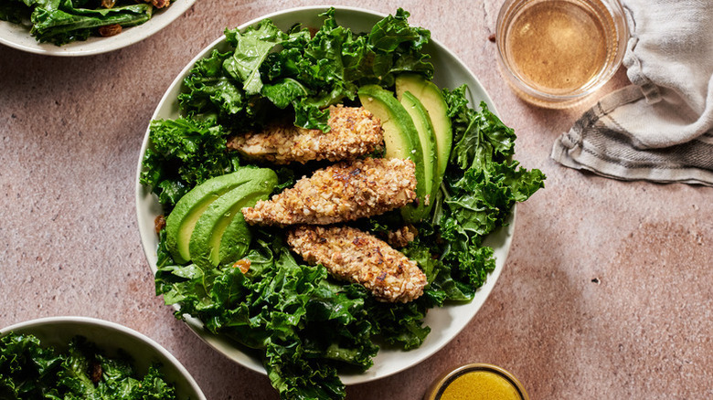 Almond-crusted chicken tenders in bowl with kale and sliced avocado