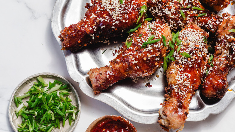 Crispy fried chicken drumsticks on plate with green onion and sesame seed garnish