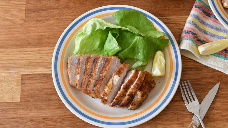 Sliced parmesan-crusted pork chops on plate with lettuce and lemon wedge
