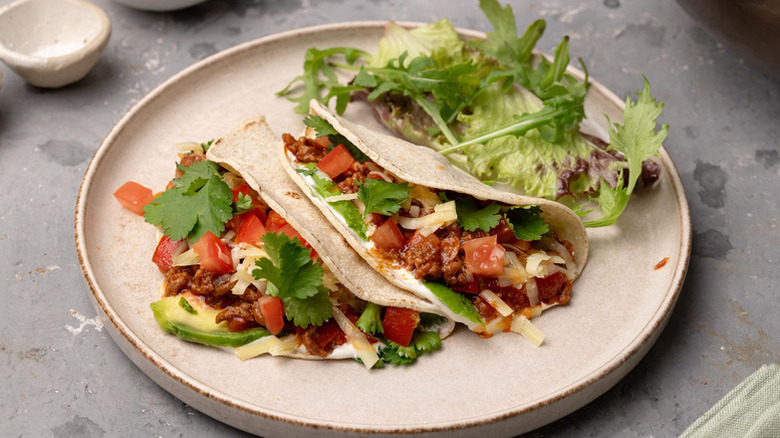Sloppy Joe tacos on plate with cilantro, tomato, and avocado
