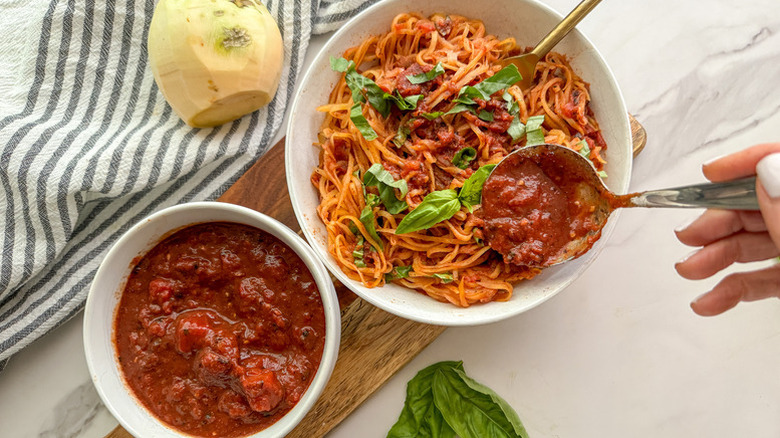 Spooning tomato sauce into bowl of spiralized rutabaga "Pasta"