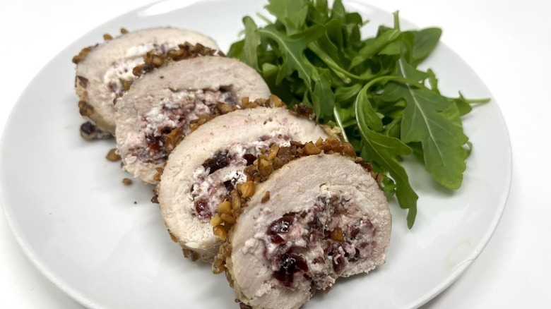 Sliced cranberry-stuffed, walnut-crusted chicken roulade on plate with fresh arugula