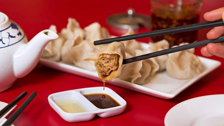 Pork and Cabbage Dumpling in chopstick being dipped in sauce