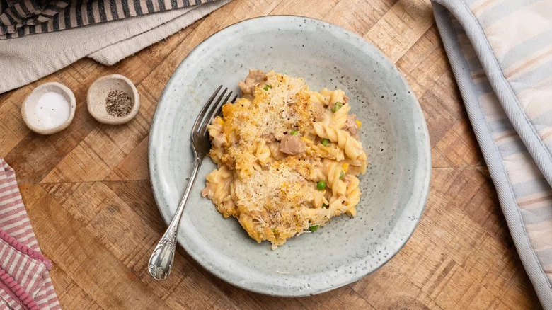 top view of cheesy tuna casserole portion with veggies served on a gray plate with salt and pepper on the side