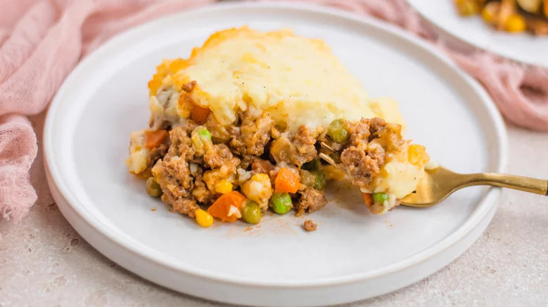 piece of shepherd's pie on a white plate with a golden fork