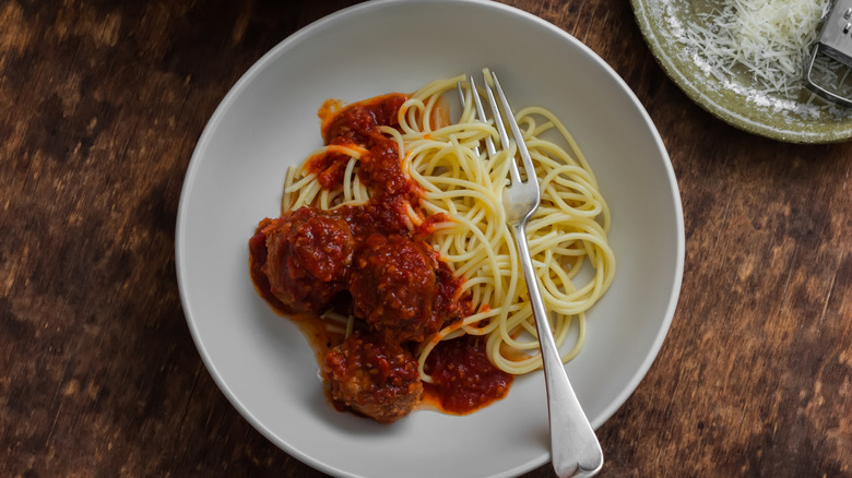 spaghetti and meatballs in plate on a wooden counter with a fork