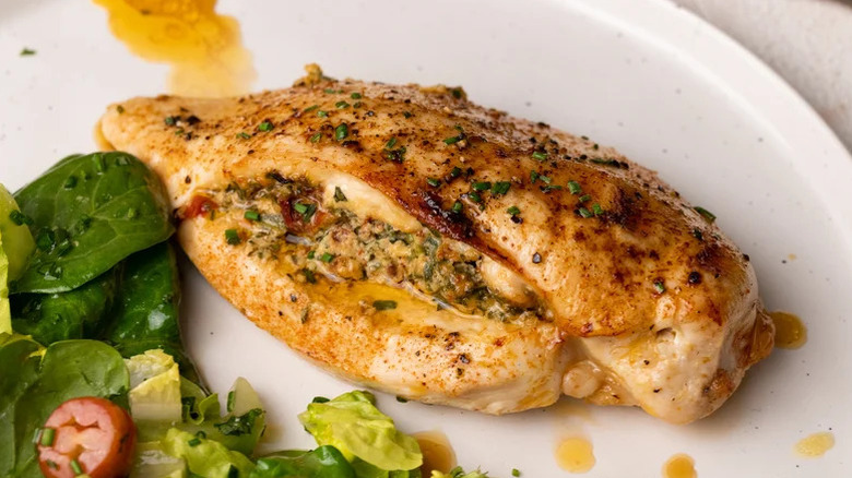 spinach and tomato stuffed chicken breast on plate with spinach and tomato salad on the side