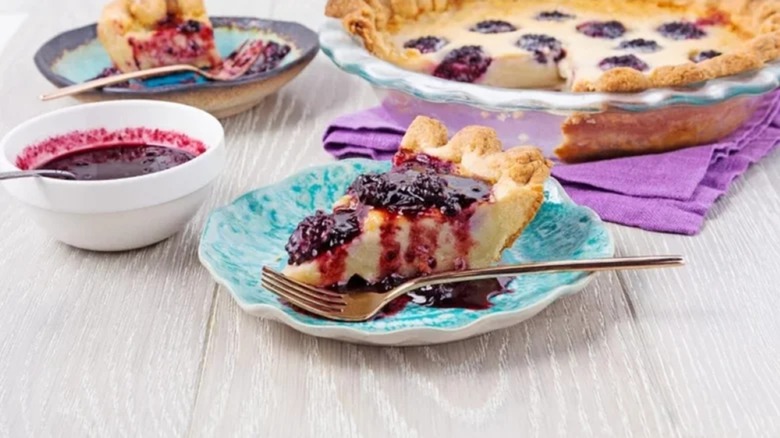 Slice of blackberry-buttermilk pie on plate with bowl of drizzle and the rest of the pie