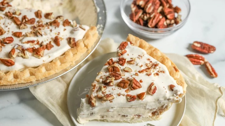 Slice of maple cream pie with pecans on plate next to the rest of the pie
