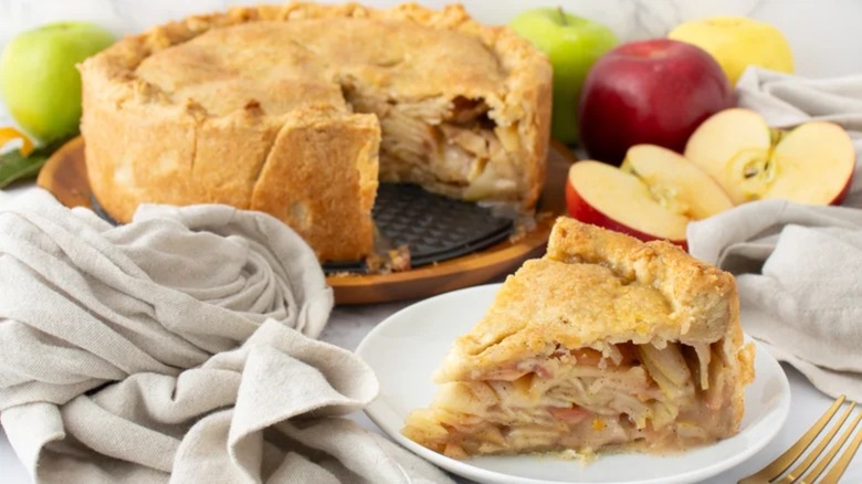 Deep dish apple pie slice with pie in background with apples
