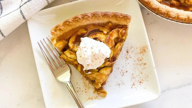 Slice of zucchini apple pie on plate with fork and whipped cream