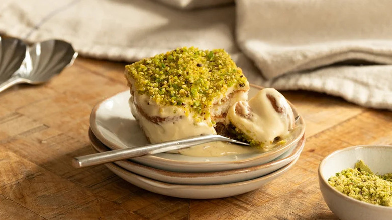 Slice of pistachio tiramisu on a stack of beige plates with one piece sliced off with a spoon