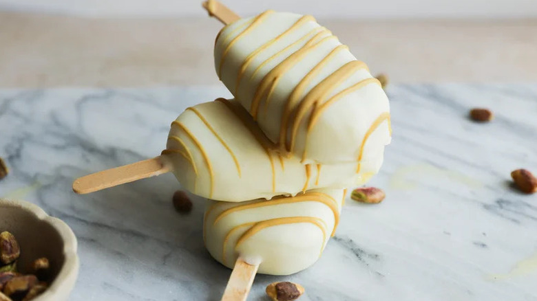 White chocolate pistachio ice pops with a pistachio drizzle stacked on marble countertop surrounded with whole pistachios