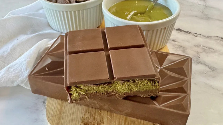 Homemade Dubai chocolate bar on wooden cutting board with pistachio cream and chocolate in the background