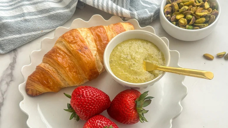 Italian pistachio cream on white plate with croissant, pistachio nuts in a bowl, and strawberries