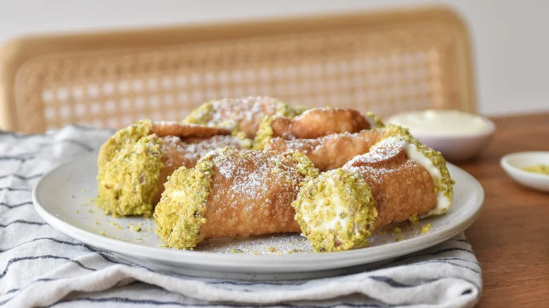 Pistachio cannoli arranged on a white plate and served on a wooden kitchen table