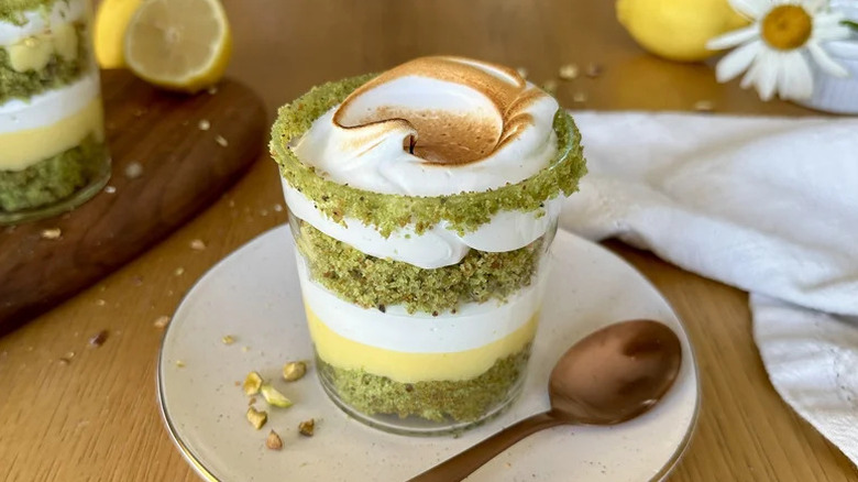 Mini lemon pistachio meringue trifle in small glass on beige saucer and a brass spoon