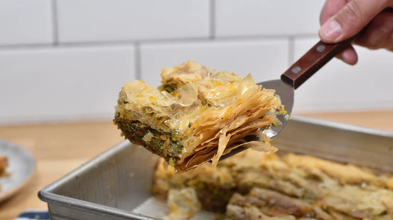 Spatula lifting pistachio and orange baklava out of metal pan