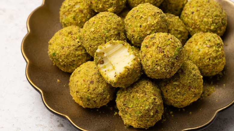 Pistachio and white chocolate truffles coated in ground pistachios stacked on brown plate with scalloped edges