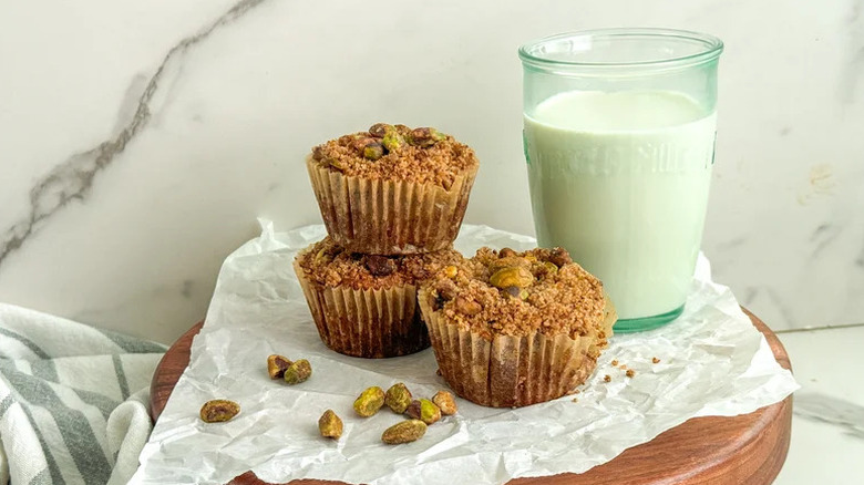 Pistachio muffins with pistachio crumble arranged on white parchment paper on wooden board with a glass of milk