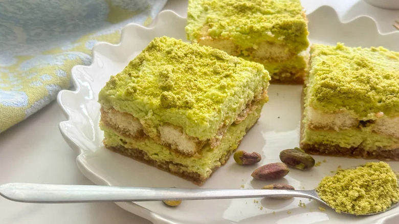 Slices of pistachio tiramisu on white plate with scalloped edges and a spoon