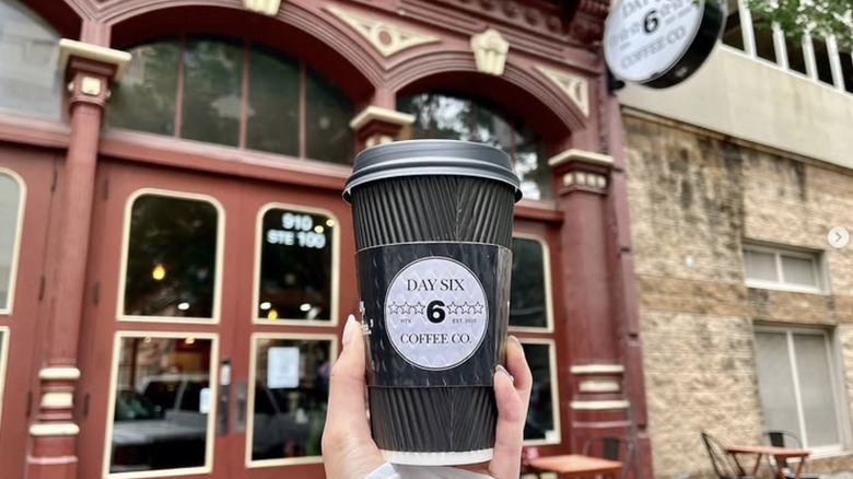 Woman holding coffee up in front of Day 6 Coffee in Houston Texas