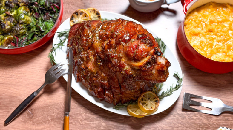 Glazed ham on plate with charred lemon rounds and rosemary sprigs