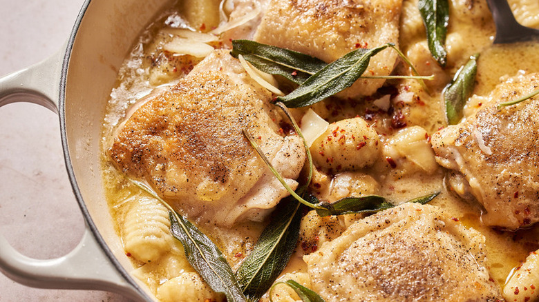 Chicken thighs and gnocchi in casserole pot with buttery sauce and sage leaves
