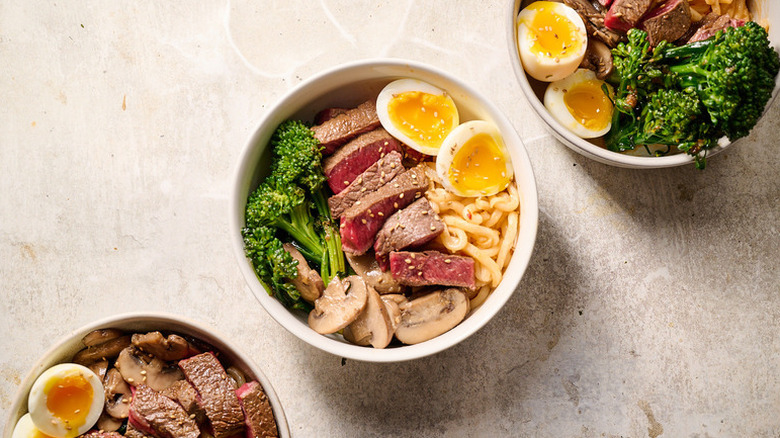 Noodle bowls with sliced beef, broccoli, and boiled eggs