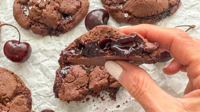 Hand holding half of a chocolate cherry-stuffed cookie
