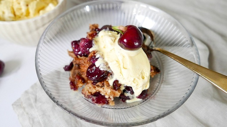 Portion of cherry dump cake in glass bowl with vanilla ice cream