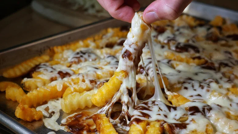 Fingers grabbing disco fries from tray with the cheese stretching