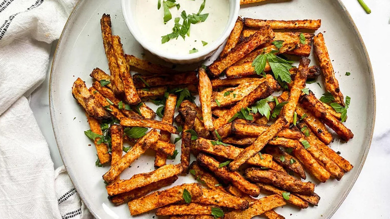 Top view of air fryer jicama fries on a white plate with white dipping sauce all sprinkled with fresh parsley