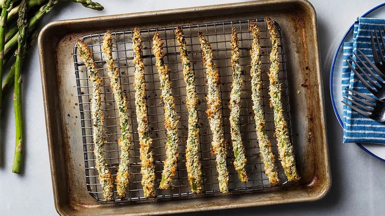 Top view of baked asparagus coated in breadcrumbs on metal baking tray