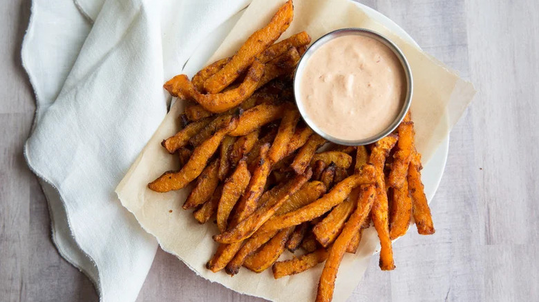Butternut squash fries served with a creamy chipotle sauce on parchment paper served on a white plate
