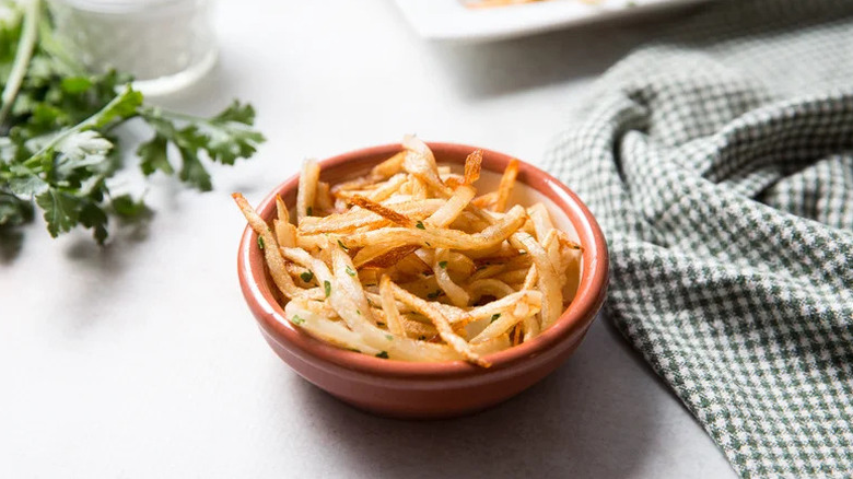 Copycat Ruth's Chris shoestring fries served in a small brown bowl with greens and a kitchen towel next to it