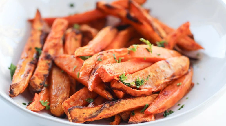 Close-up image of air fryer sweet potato fries sprinkled with parsley and served on white plate