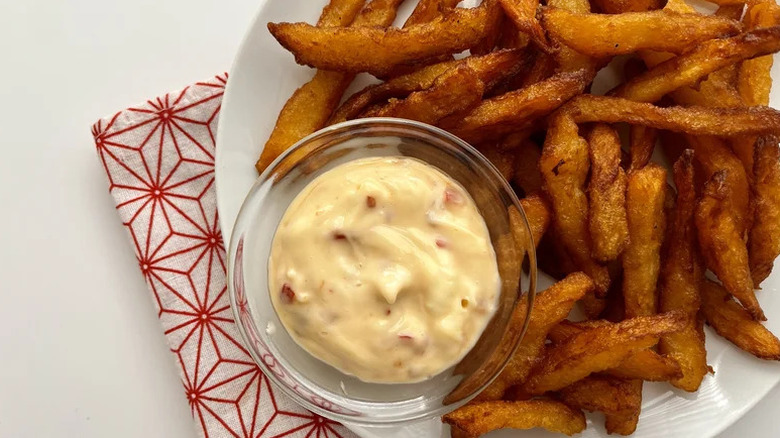 Top view of rutabaga fries on white plate with a dipping sauce served in a glass bowl on the side