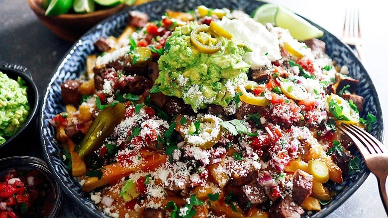 Carne asada fries served in a big serving bowl with guacamole, cheese, and jalapenos on top