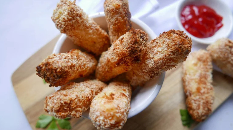 Halloumi fries in small white cup on wooden board with sauce on the side in the background