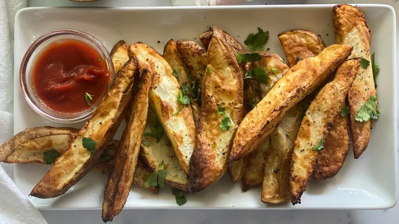 Homemade air fryer steak fries with ketchup on white plate sprinkled with green herbs