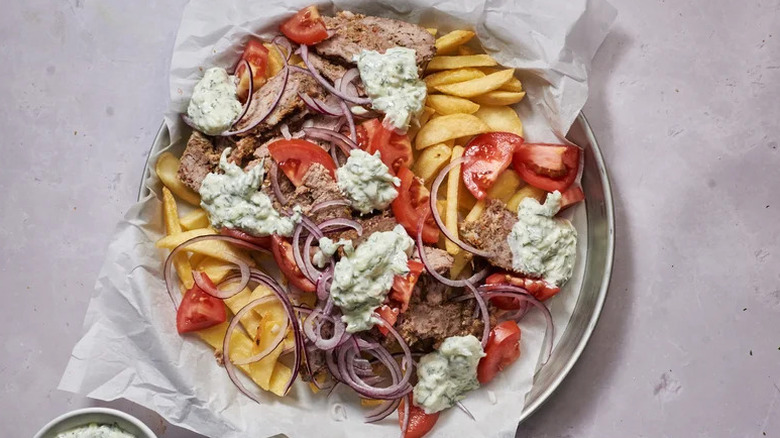 Loaded gyro fries on parchment paper on metal tray topped with onions, chunky sauce, and tomatoes