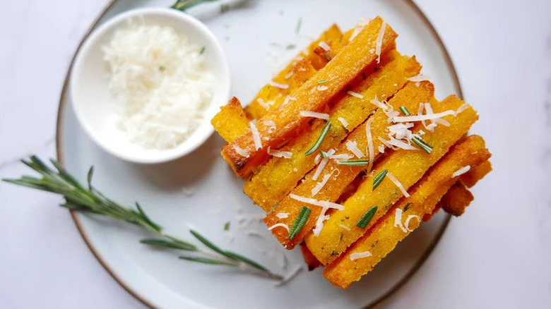 Oven-roasted polenta fries on white plate with rosemary sprinkled with some grated cheese