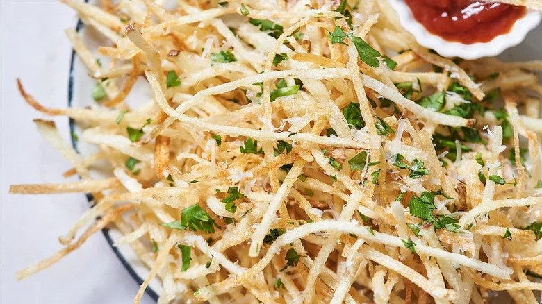 Shoestring garlic Parmesan fries topped with parsley on plate with a red sauce on a plate