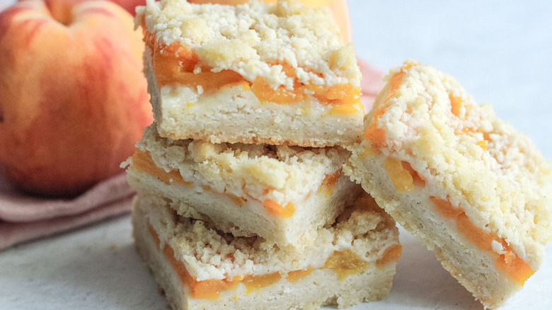 Stack of peach crumble bars with fresh peach in background